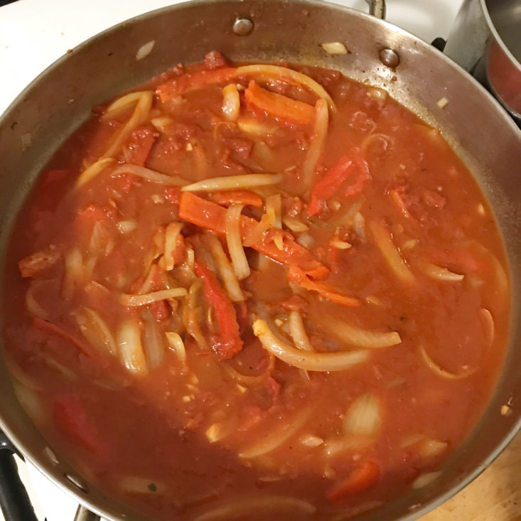 sliced onions and peppers sauteing in pan with crushed tomatoes