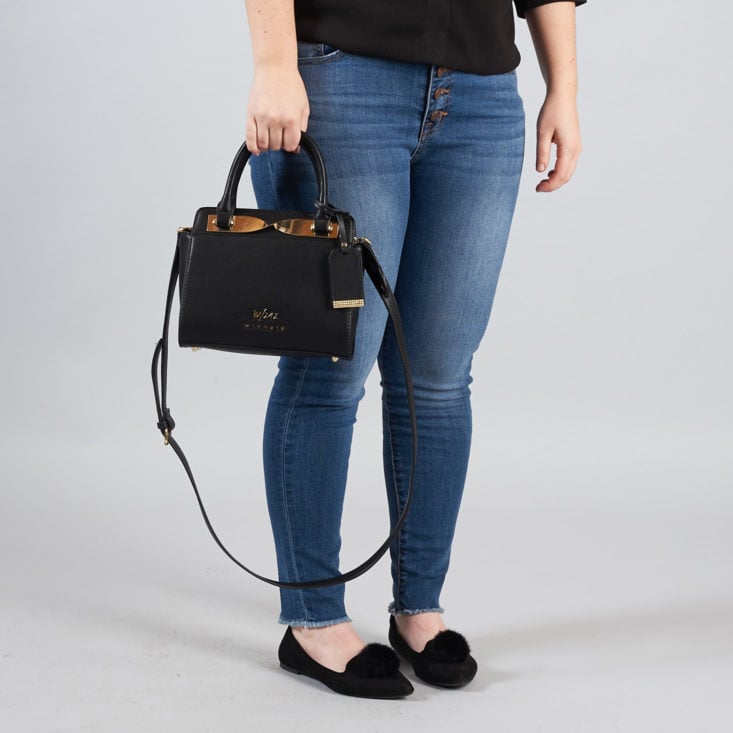 woman holding a black handbag with a shoulder strap and regular handles