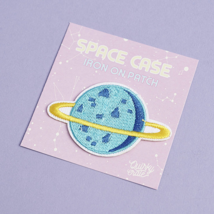 a patch shaped like a blue moon with a yellow ring around it on a package that says "Space Case"
