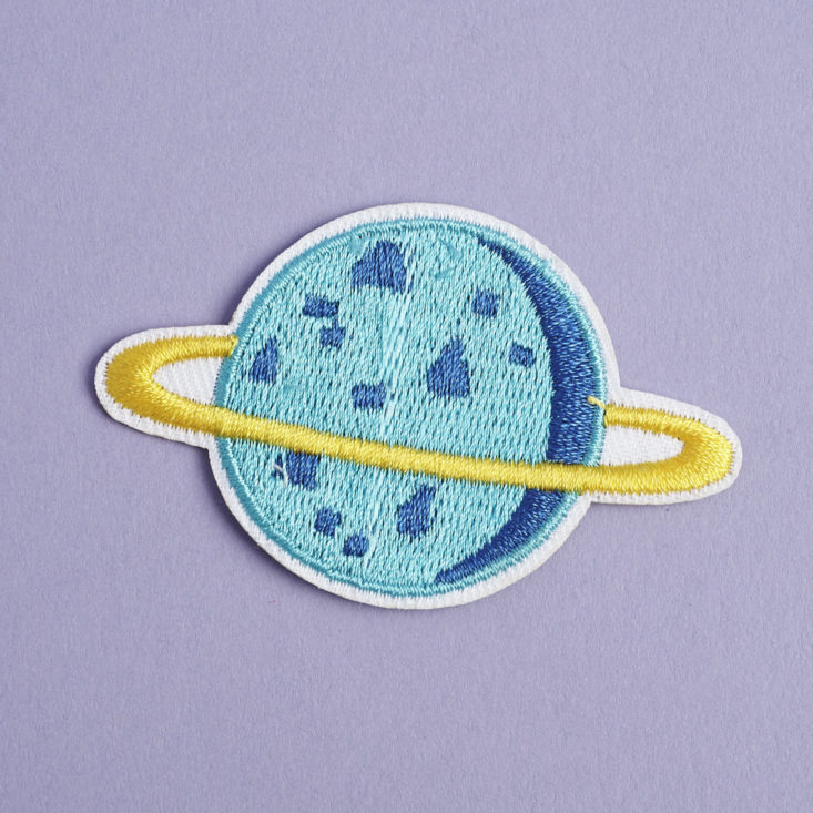 small blue embroidered patch that looks like a moon with a ring around it