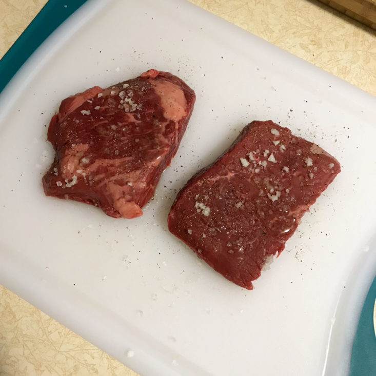 salt and peppered steaks on cutting board