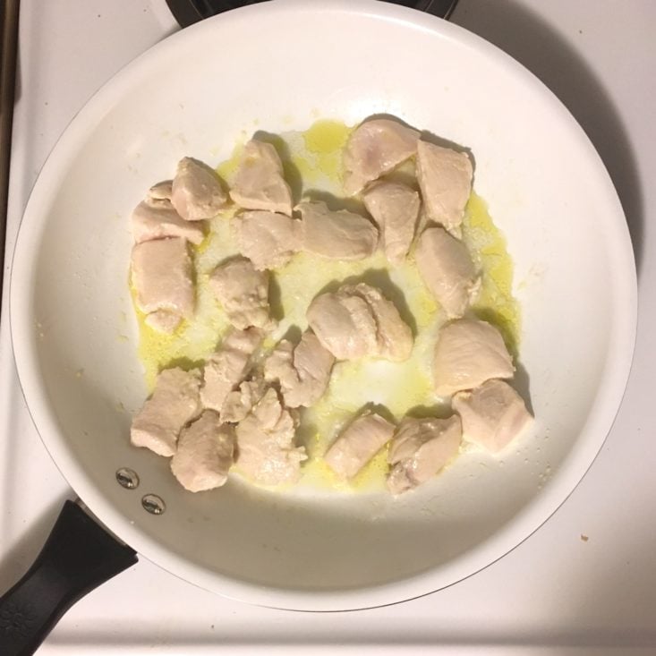 diced chicken cooking in a large white skillet for the cajun chicken grits recipe