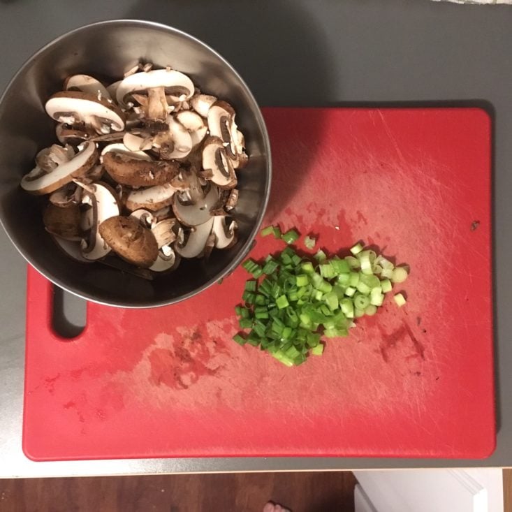 chopped mushrooms and sliced green onions on a red cutting board, prepped for the cajun grits recipe